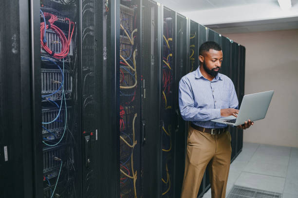 istock Shot of a young man using a laptop while working in a server room 1347879800