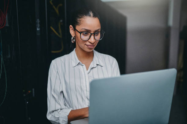 istock Shot of a young woman using a laptop while working in a server room 1347879840