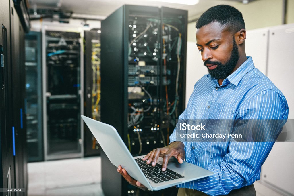 Shot of a young man using a laptop while working in a server room I have a plan to repair this Technology Stock Photo