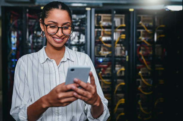 istock Shot of a young woman using a cellphone while working in a server room 1347879992