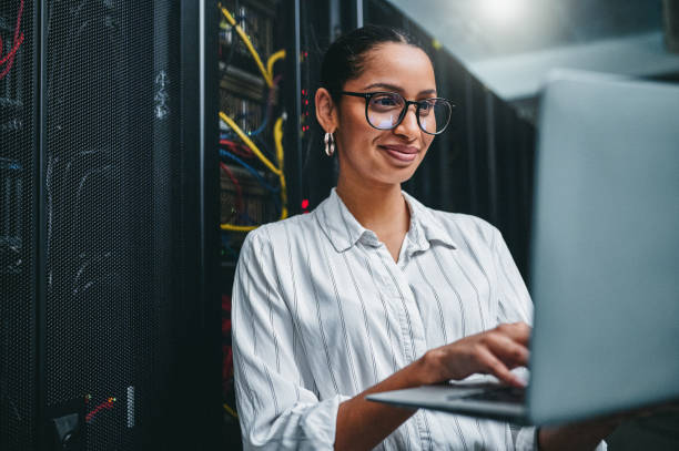 tiro de uma jovem usando um laptop enquanto trabalhava em uma sala de servidor - data center computer programmer women - fotografias e filmes do acervo