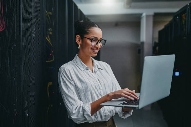 istock Shot of a young woman using a laptop while working in a server room 1347880014