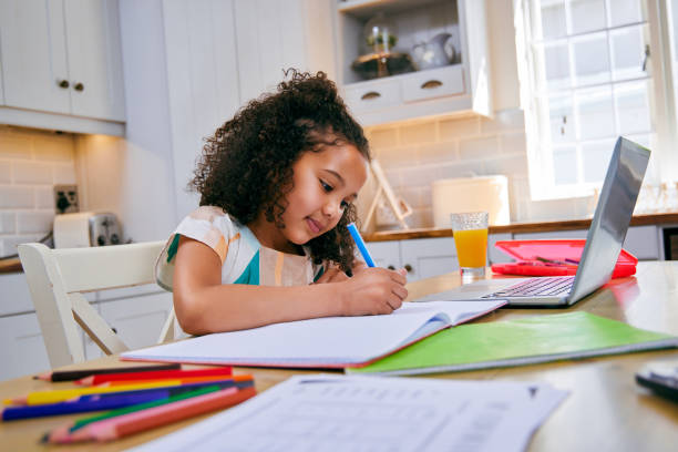 istock Shot of a young girl completing her homework in her kitchen using a laptop 1347880048