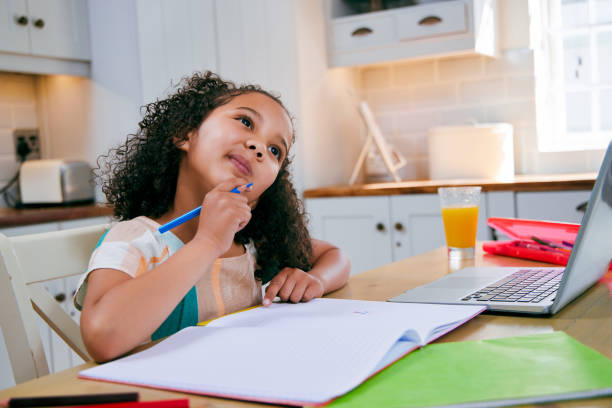 istock Shot of a young girl completing her homework in her kitchen using a laptop 1347882620