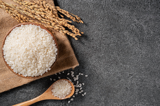 White raw rice in a bowl with the ear on the dark black table background.