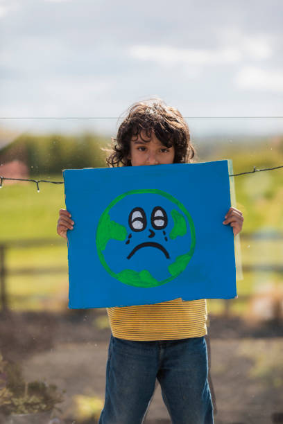 Be Sustainable! Boy standing holding a sign with the earth painted on it with a face that is crying. He is an activist for a more sustainable world in the North East of England. peace demonstration stock pictures, royalty-free photos & images