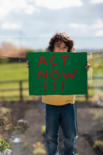 Boy standing holding a sign with the words 'Act Now!' painted on it. He is an activist for a more sustainable world in the North East of England.