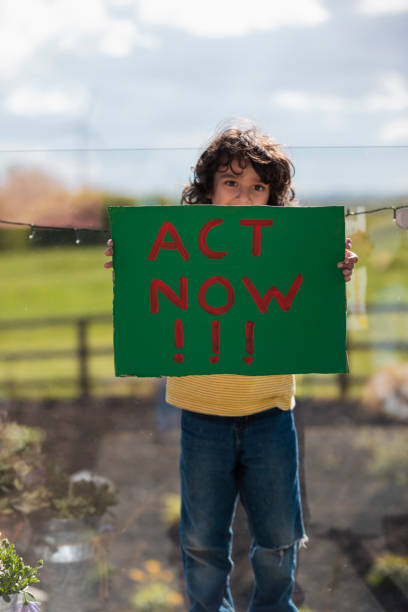 Act Now! Boy standing holding a sign with the words 'Act Now!' painted on it. He is an activist for a more sustainable world in the North East of England. peace demonstration stock pictures, royalty-free photos & images