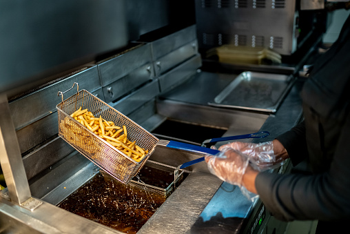 Female hands holding a frying pan with french fries at a commercial kitchen