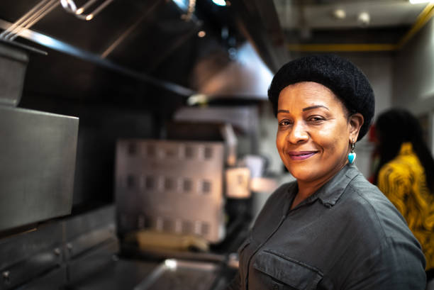 retrato de uma mulher madura em uma cozinha comercial - owner small business restaurant african ethnicity - fotografias e filmes do acervo