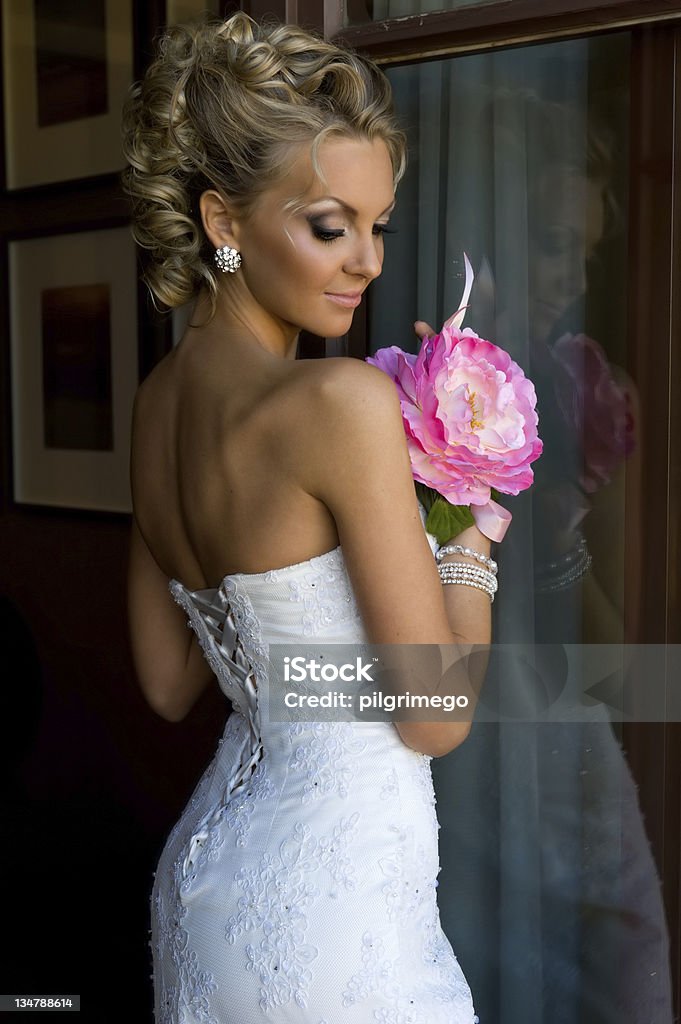 Beautiful bride with bunch of flowers. Beautiful bride is standing at the window with bunch of flowers. Adult Stock Photo