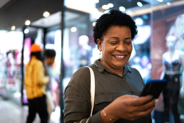 mature woman using a smartphone at the mall - telephone indoors retail shopping mall imagens e fotografias de stock