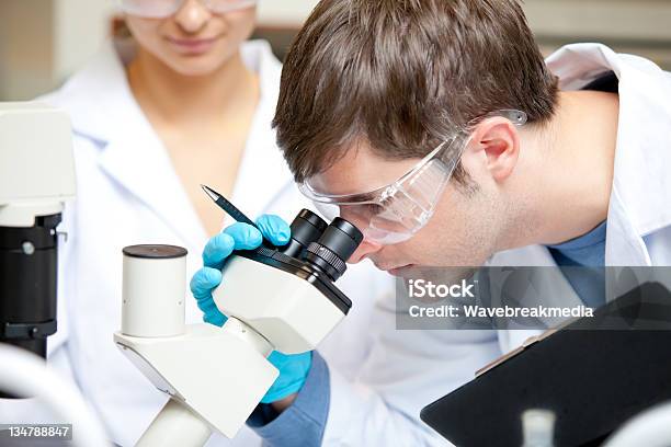 Caucasian Male Scientist Holding Pen And Clipboard Looking Throu Stock Photo - Download Image Now