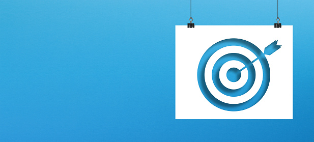 Target sign on paper hanging with clip on blue background. Horizontal composition with copy space.