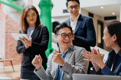 Image of a team of excited Asian business professionals cheering and celebrating business success in office