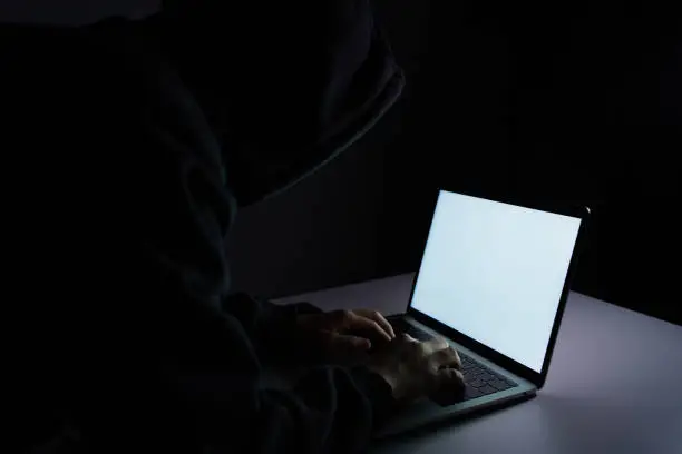 hooded hacker stealing data from laptop at night.