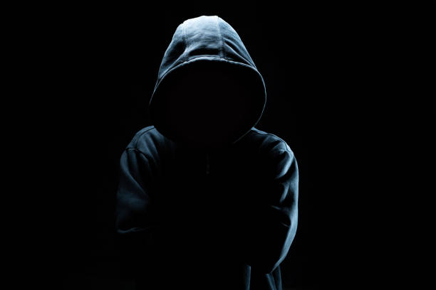 Computer hacker in black mask and hoodie. Obscured dark face. Data thief, internet fraud, cyber security concept. Computer hacker in black mask and hoodie. Obscured dark face. Data thief, internet fraud, cyber security concept. thief stock pictures, royalty-free photos & images