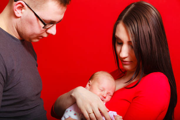 Family, childhood and parenthood concept. Little newborn baby sleeping on mother chest, father standing with them.