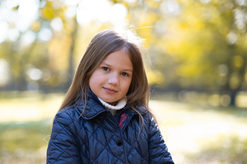 Autumn portrait of cute little blond girl in city park. Beautiful smiling child having fun outdoors on a warm fall day. Autumn kids fashion, seasonal sales.