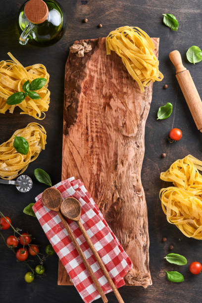 Tagliatelle. Homemade pasta, basil leaves, flour, pepper, olive oil, cherry tomato and rolling pin and pasta knife on dark old wooden background. Food concept. Mock up. Horizontal with copy space.