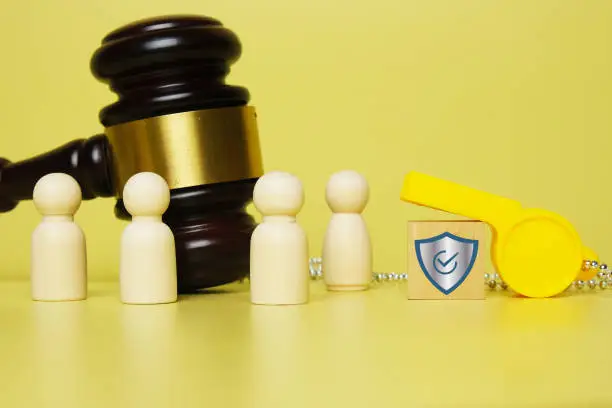 A picture of peg doll men and women, whistle, gavel and shield on wooden block. Protect the whistleblower concept