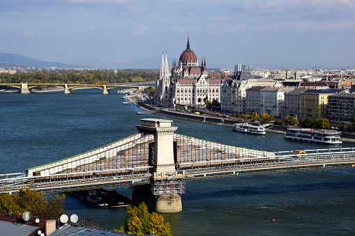 Aerial view of the Chain bridge in Budapest under construction. undergoing repair and renovation. summer scene. panoramic view of the Danube and the Parliament. blue sky. tour boats by the river shore