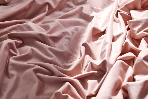 Pink wrinkled bedding with morning light, book and candle. Self care and relaxation background.