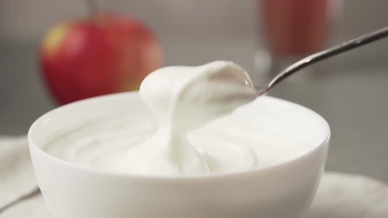 Hand picks up yogurt with a spoon. Bowl of greek yogurt with apple and glass of juice.