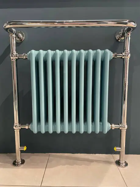 Stock photo showing an old fashioned Victorian-style, blue radiator and heated towel rail in front of grey painted wall of a modern, luxury bathroom.