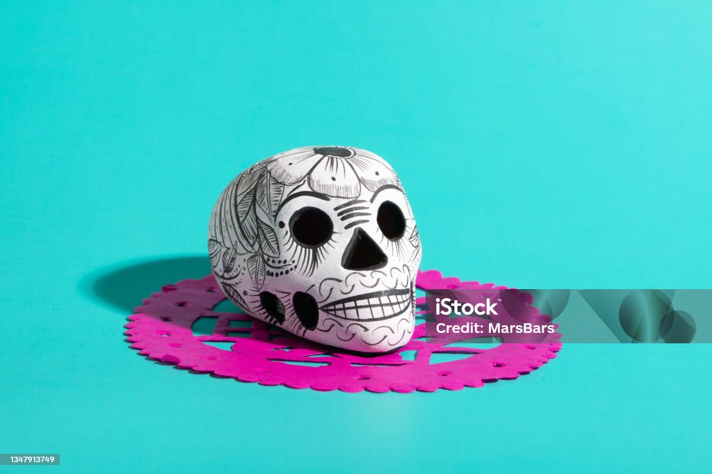 Day of the dead pottery skull (calavera) on hot pink papel picado on teal blue background, Dia de Muertos background Altar Stock Photo