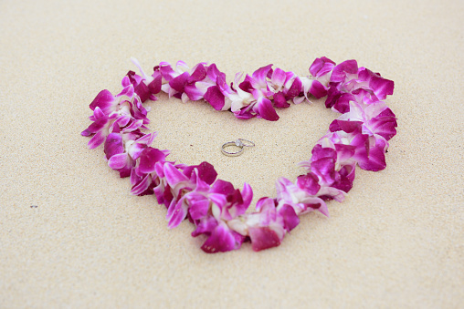 Stock photo showing close-up view of heart shape of seashells on a sunny, golden sandy beach with sea at low tide in the background. Romantic holiday and honeymoon concept.