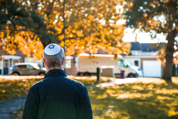 Jewish man wearing skull cap walking on residential street Color image depicting a mid adult Jewish man in his 30s wearing a traditional Jewish skull cap (with star of David design). Rear view of the man as he walks on a residential city street, with houses defocused in the background. yarmulke photos stock pictures, royalty-free photos & images