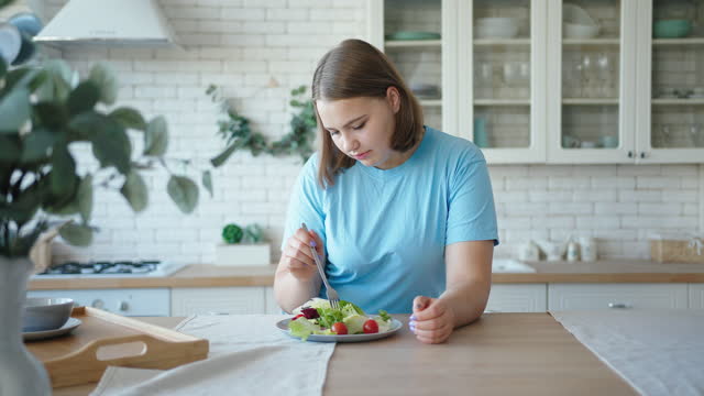 Plump woman eats vegetable salad standing in kitchen