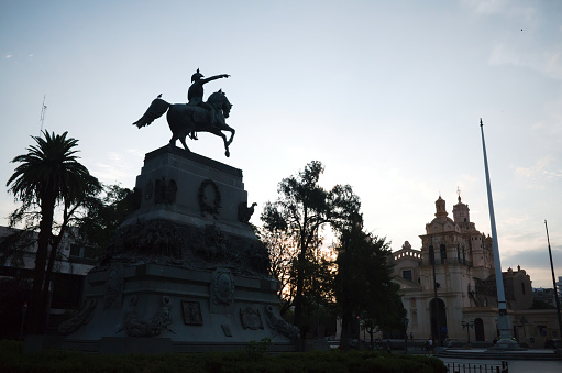 Cordoba, Argentina - January, 2020: Silhouette of statue of General San Martin on horseback in Plaza San Martin at dusk. Cathedral called Catedral de Cordoba on background. Historic center of Cordoba