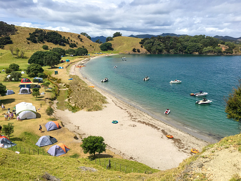 View of campsite on Urupukapuka Island, boats in the bay, golden sand, summer feeling, Bay of Islands, NZ
