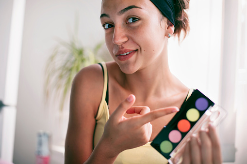 Portrait of а happy girl showing makeup palette while recording her video. Girl making a video for her vlog about cosmetics. Influencer marketing. Social media concept.