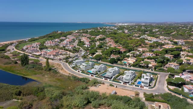 Aerial overview of Quinta do Lago resort buildings in Vale de Lobo, Algarve, Portugal, Europe. Shot of rooftops of luxury cottages in green landscape with mountains on background. Golf fields.