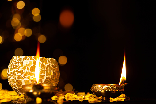 Brass Golden Diya Illuminated golden bokeh Black Background and decorative pot. Indian Festival Diwali Pooja, Navratri, Dussehra Puja, New Year, Deepawali Or Shubh Deepavali