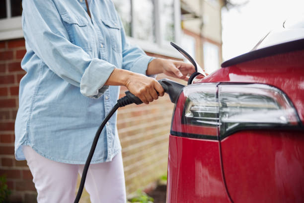 close up of woman attaching charging cable to environmentally friendly zero emission electric car at home - electric plug electricity power cable imagens e fotografias de stock