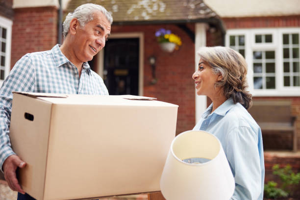 Portrait Of Mature Couple Carrying Boxes On Moving Day In Front Of Dream Home Portrait Of Mature Couple Carrying Boxes On Moving Day In Front Of Dream Home downsize stock pictures, royalty-free photos & images