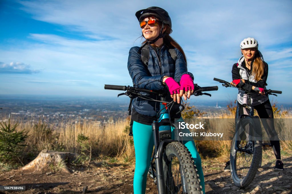 Two young women on a e-bike ride Photo of two cheerful young women on a bike ride on a beautiful autumn sunny day. These are electric enduro mountain bicycles. Mountain Biking Stock Photo