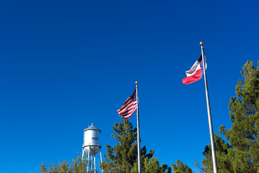 Marfa, TX: US and Texas Flags Blowing in Blue Sky, Marfa Water Tower. Copy space available.