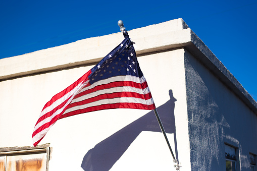 Marfa, TX: US Flag Blowing Against White Building, Blue Sky. Copy space available.