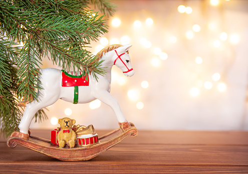 Vintage retro toy horse on wooden table with fir branches on background of bokeh lights. Copy space. Greeting card, happy new year and merry Christmas.