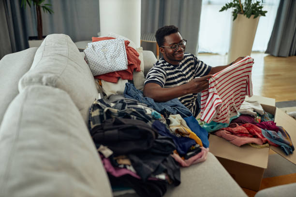 istock Young black man sorting clothes indoors at home, charity donation concept 1347954094