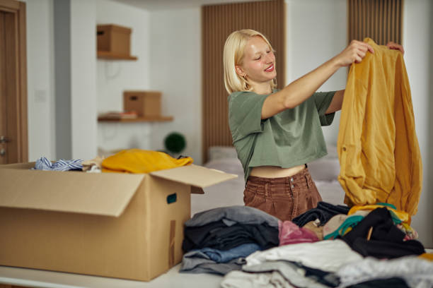 istock Woman folding and packing used clothes into cardboard donation box. 1347954814