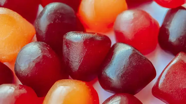 Photo of Close-up texture of red, orange and purple multivitamin gummies on white background. Healthy lifestyle concept