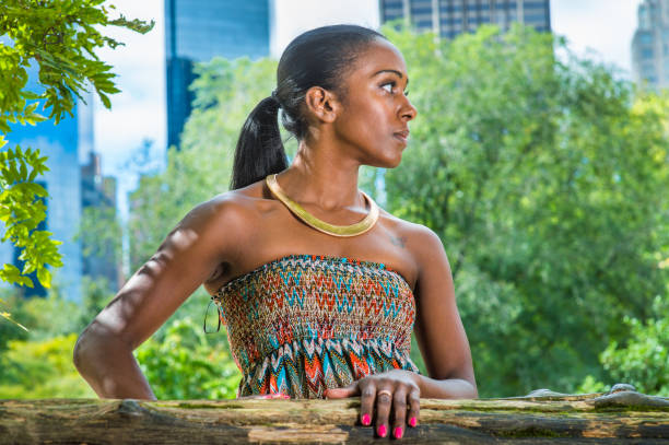 une jeune femme noire debout à l’extérieur dans un parc à new york, détournant le regard - women dress black young women photos et images de collection