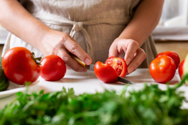 istock Chef slicing tomato using knife on the table in restaurant. Process of cutting and preparation food in kitchen. 1347958256