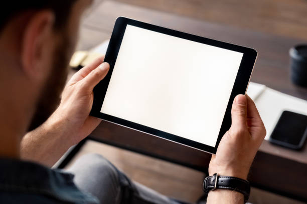 istock Man holding digital tablet device white screen in hand view over shoulder 1347959353